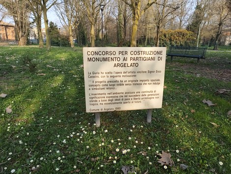 Monumento ai partigiani di Argelato, circondato da un'area verde e alberi, con un cartello informativo.
