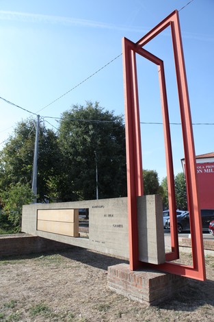 Monumento ai Caduti di Manzolino, struttura moderna con elementi in pietra e acciaio, circondato da verde.