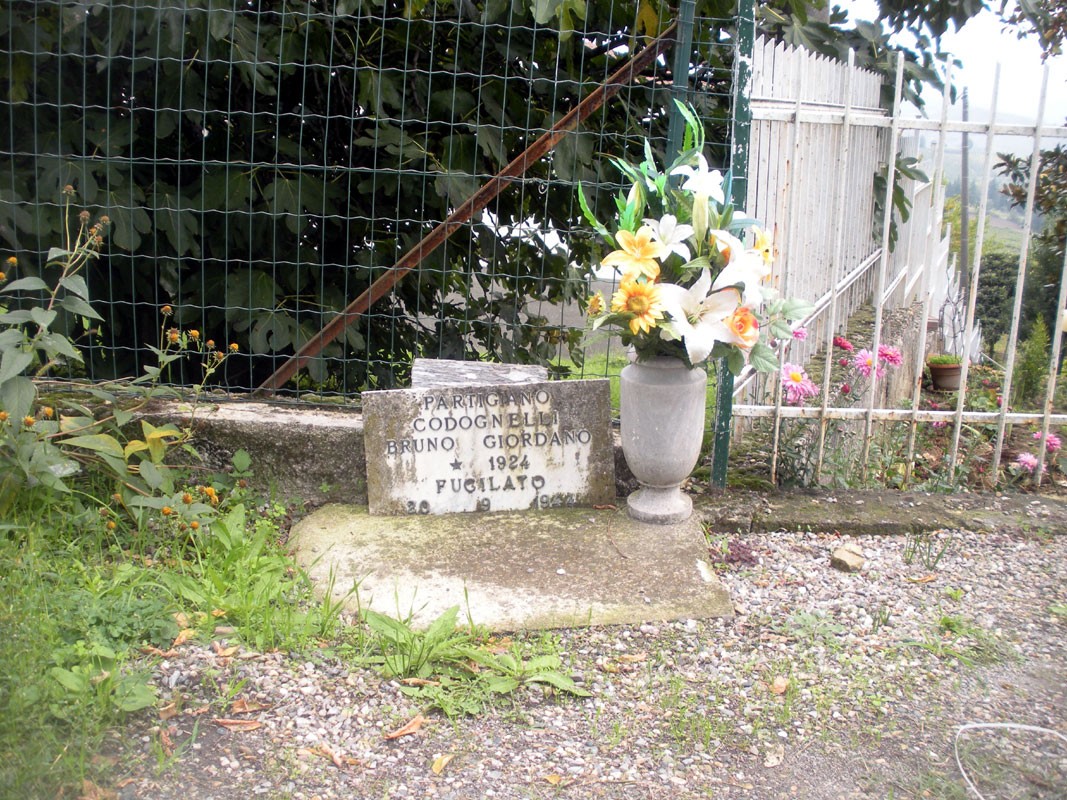 Lapide commemorativa a Codognelli con fiori e decorazioni in un contesto naturale.