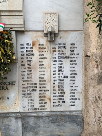 Monumento ai Caduti di Alghero, con incisioni commemorative e decorazioni floreali.