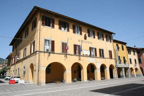 Edificio del Municipio con archi, finestre e bandiere, situato in una piazza soleggiata.