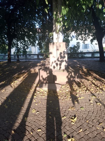 Lapide commemorativa ai caduti per la Resistenza, circondata da alberi e foglie, in un'atmosfera di rispetto e commemorazione.