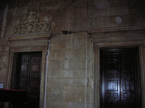 Due porte di legno scuro su una parete in pietra, con decorazioni in alto e dettagli architettonici.