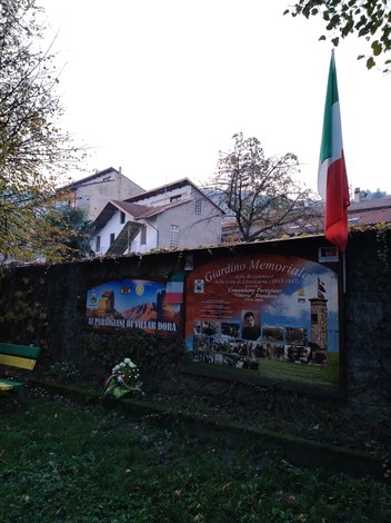 Giardino memoriale a Blandino, con manifesti commemorativi e la bandiera italiana in un contesto naturale e tranquillo.