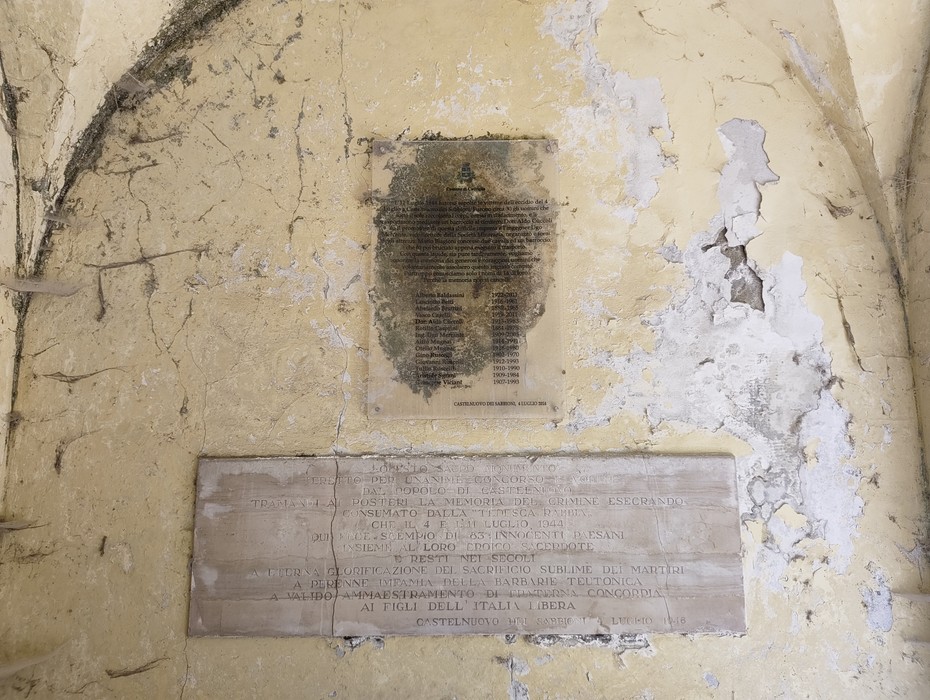 Due lapidi con iscrizioni su parete intonacata, una annerita in alto e una in marmo più leggibile in basso.