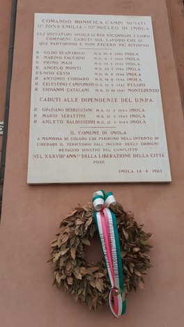 Lapide commemorativa dedicata agli sminatori caduti, situata a Imola, con omaggio floreale.