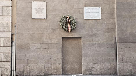 Lapide commemorativa su un muro con una corona di alloro, in ricordo di eventi storici e persone significative.