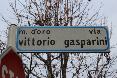 Targa stradale con il nome di via Vittorio Gasparini, contornata da alberi spogli.