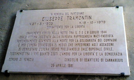 Lapide commemorativa dedicata a Giuseppe Tramontin, partigiano, con iscrizioni su un fondo chiaro.