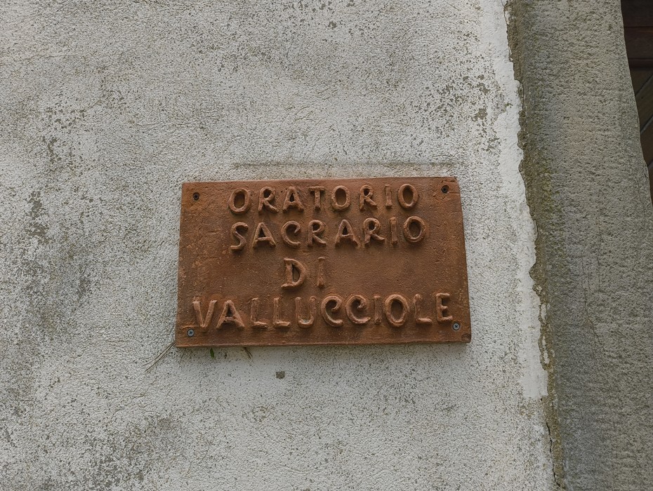 Insegna in bronzo che indica l'Oratorio di Vallucciole, immerso nella natura circostante.