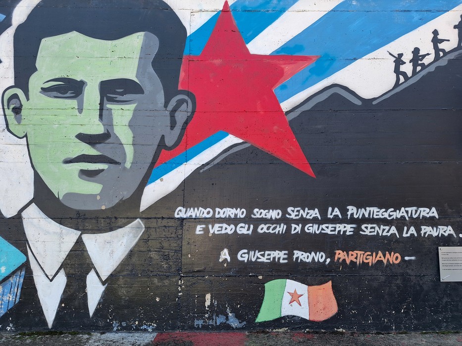 Murale con volto di partigiano, stella rossa e montagne stilizzate sullo sfondo, con iscrizione dedicata a Giuseppe.