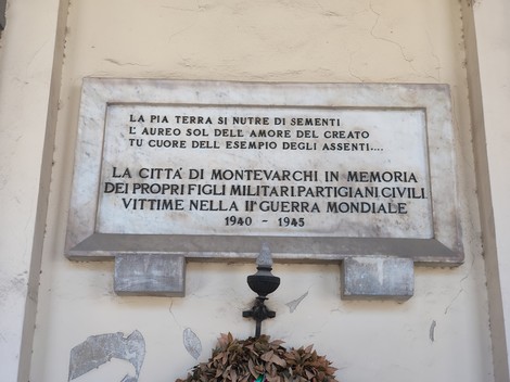 Lapide marmorea con iscrizione, fissata su una parete, con mensola e corona di foglie sottostante.