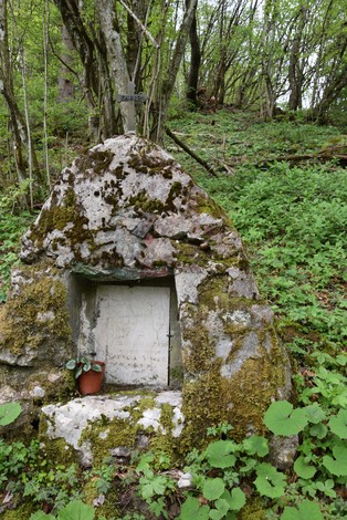 Cippo di pietra nel bosco, ricoperto di muschio e circondato da vegetazione lussureggiante.