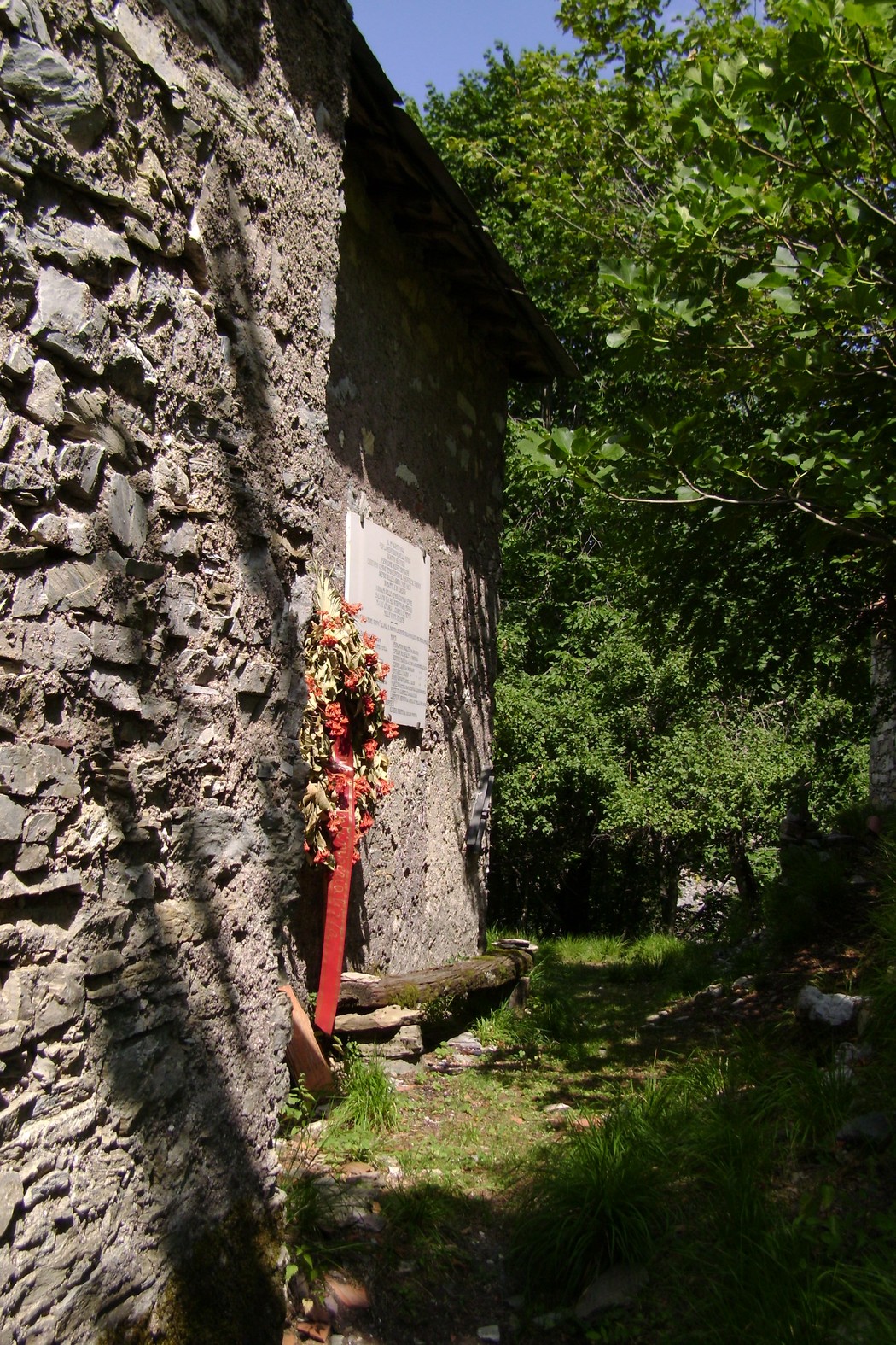 Lapide commemorativa del Gruppo Valanga, circondata da vegetazione, su una parete in pietra.