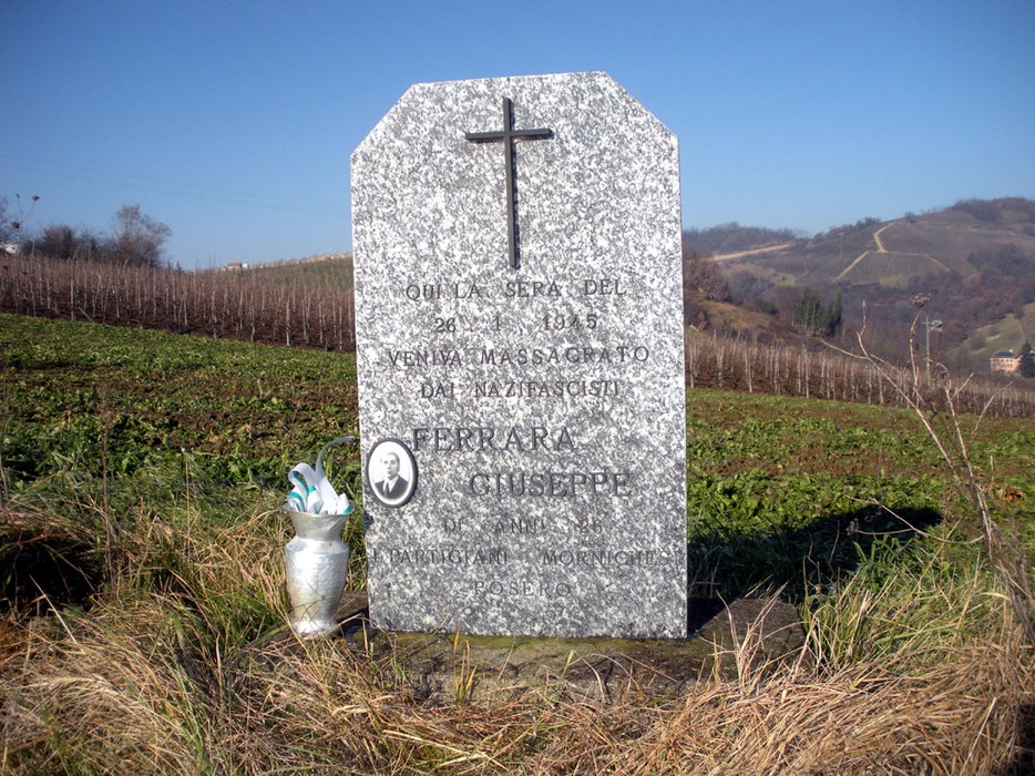 Cippo commemorativo a Ferrara, con dedicazioni e simboli religiosi in un contesto naturale.