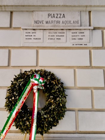 Lapidi commemorative dedicate ai nove martiri aquilani, con una corona di alloro e nastro tricolore.