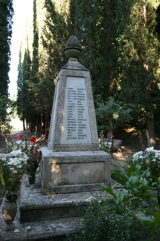 Monumento commemorativo dedicato alle vittime dell'eccidio di Guardistallo e Montescudaio, circondato da piante.