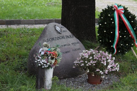 Cippo commemorativo a Sonzogni, con fiori e decorazioni, immerso nel verde.