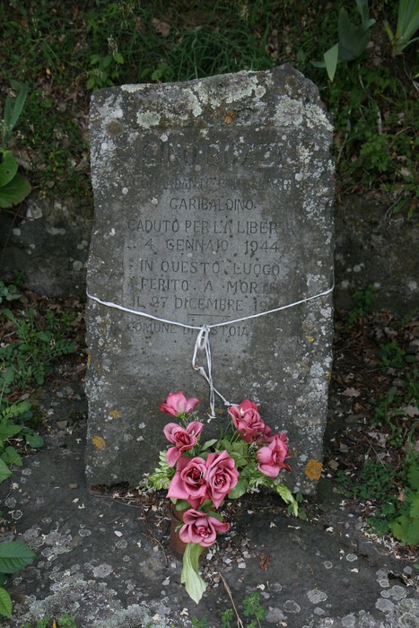 Cippo commemorativo a Bozzi in memoria di un partigiano, adornato con fiori artificiali.