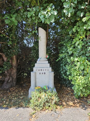 Cippo commemorativo circondato da vegetazione, dedicato ai martiri dell'eccidio dell'Aeroporto di Forlì.