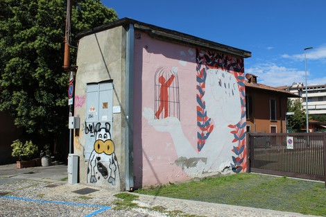 Murale colorato su un muro di edificio, con figure stilizzate e motivi floreali in un contesto urbano.