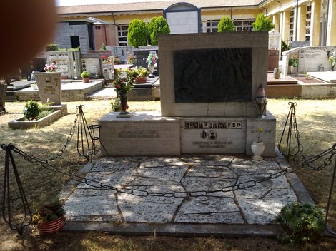 Monumento commemorativo ai caduti della Guerra di Liberazione, situato in un cimitero, con fiori e decorazioni.