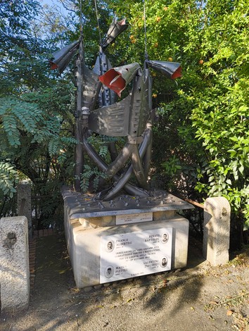 Monumento in memoria di Bartolini, Pizzoli, Zuppiroli e Albertini, circondato da vegetazione.