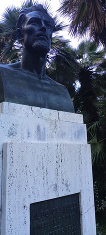 Monumento a Gastaldi con busto in bronzo circondato da vegetazione lussureggiante.