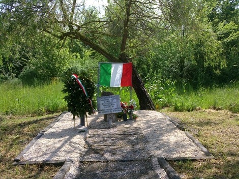 Cippo commemorativo a Braghini e Martuccello, con bandiera italiana e decorazioni floreali, immerso nel verde.