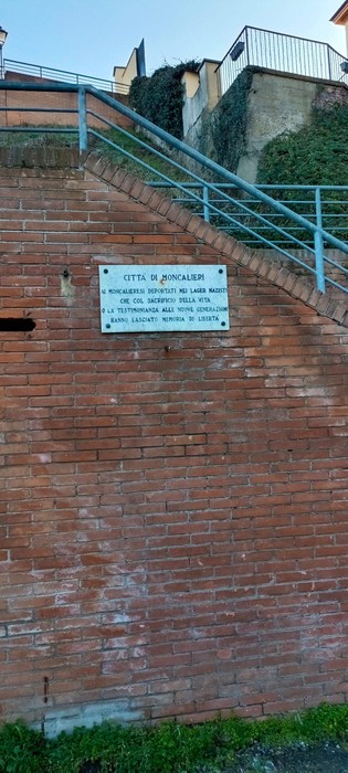 Lapide commemorativa dedicata ai deportati, affissa su un muro storico in un contesto urbano.
