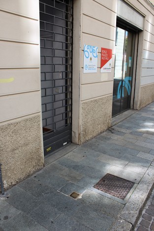 Pietra d'inciampo dedicata a Stella, situata davanti a un edificio con vetrine e grate di sicurezza.