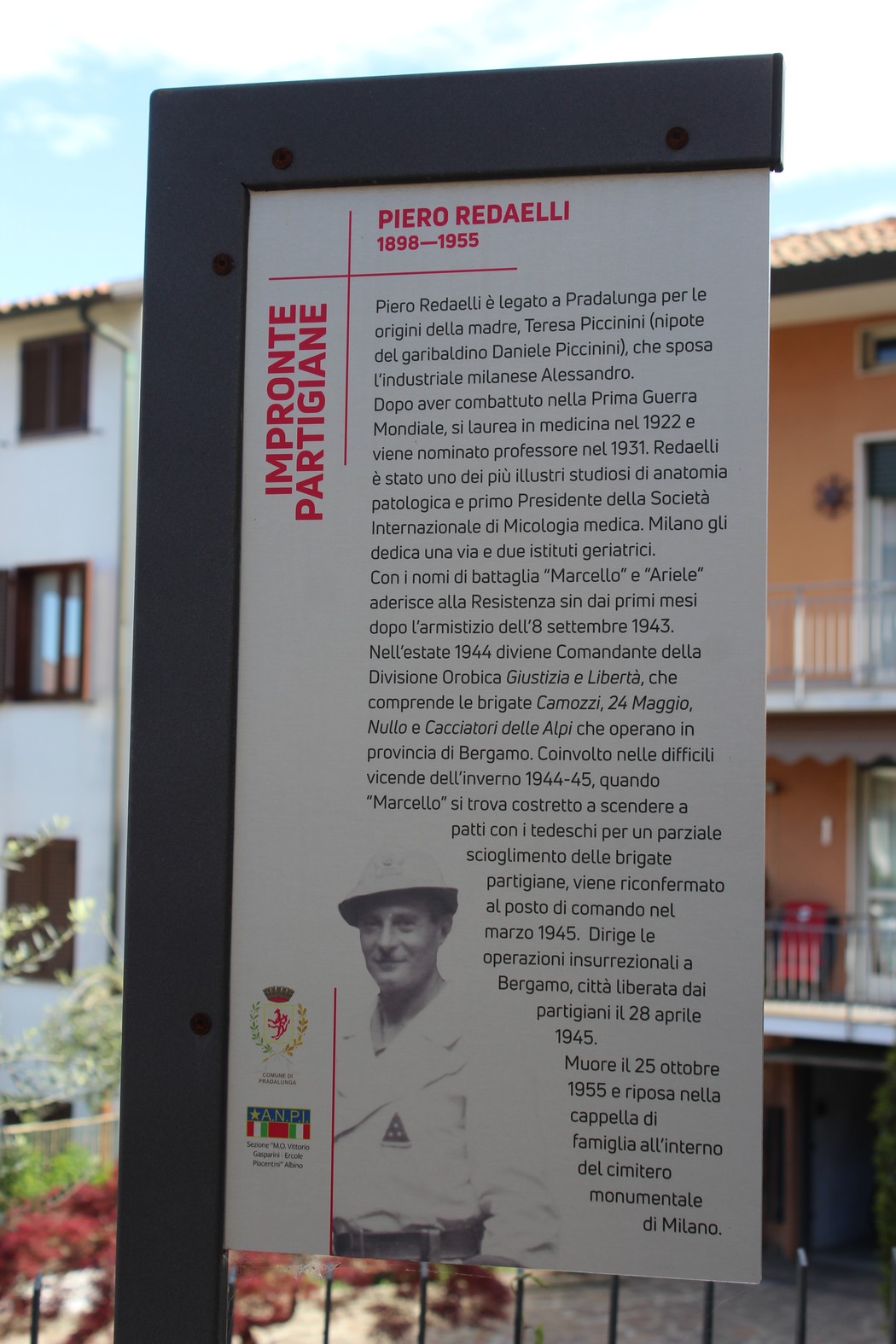 Impronta partigiana dedicata a Piero Redaelli, con pannello informativo e sfondo di un edificio.