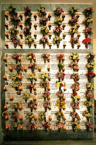 Cripta dei Deportati con lapidi e immagini commemorative decorate da fiori artificiali.