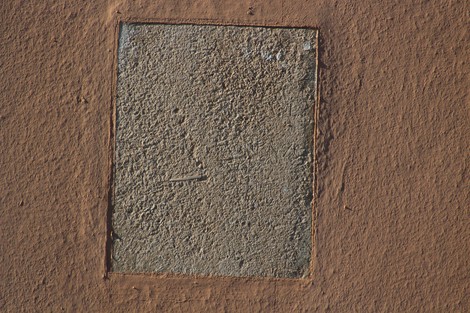 Lapide in pietra grigia inserita in una parete di terra cotta, con evidenti segni di usura e deterioramento.