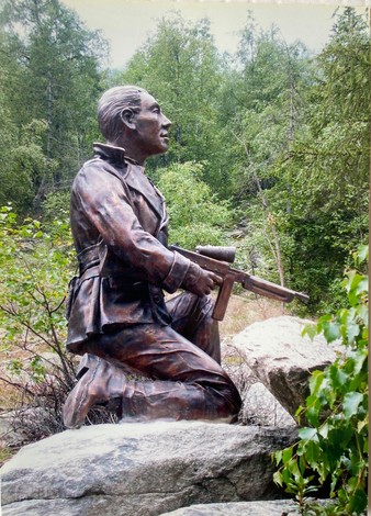 Monumento a Ilardi, statua bronzea di un soldato inginocchiato tra la vegetazione e le rocce circostanti.