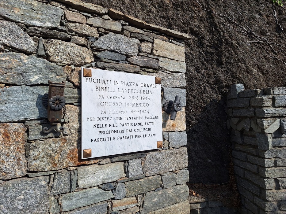 Lapide marmorea con iscrizione fissata su un muro in pietra a vista.