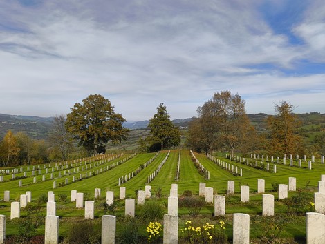 Cimitero di guerra sudafricano con file di tombe bianche su un prato verde, circondato da alberi e colline.