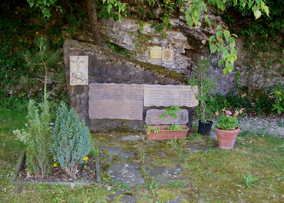 Area monumentale ai Caduti di Partina, con stele commemorativa e decorazioni floreali in un contesto naturale.