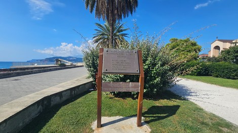 Targa commemorativa dedicata ai caduti per la libertà, situata in un'area verde vicino al mare.