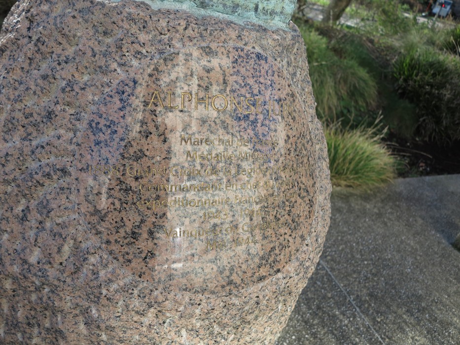 Busto di Juin, scultura in pietra con iscrizioni, immersa nella natura circostante.