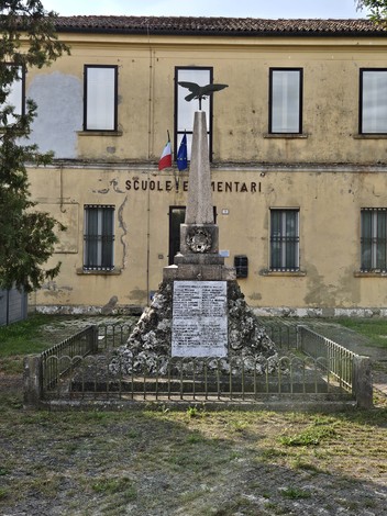 Monumento ai Caduti di Coccanile, situato davanti a una scuola, con decorazioni e una cornice di alberi.
