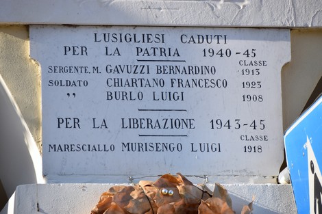 Lapide in marmo su parete esterna, con iscrizione ai caduti, sormontata da una corona di foglie secche.