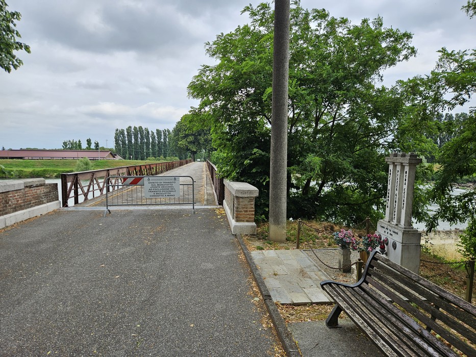 Ponte chiuso con barriera, panchina in legno e verde circostante, verso il fiume a Bocci, Piazza e Meda.