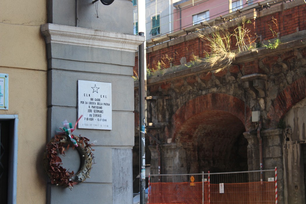 Lapide commemorativa con decorazioni natalizie, situata in un contesto urbano, vicino a archi in pietra.