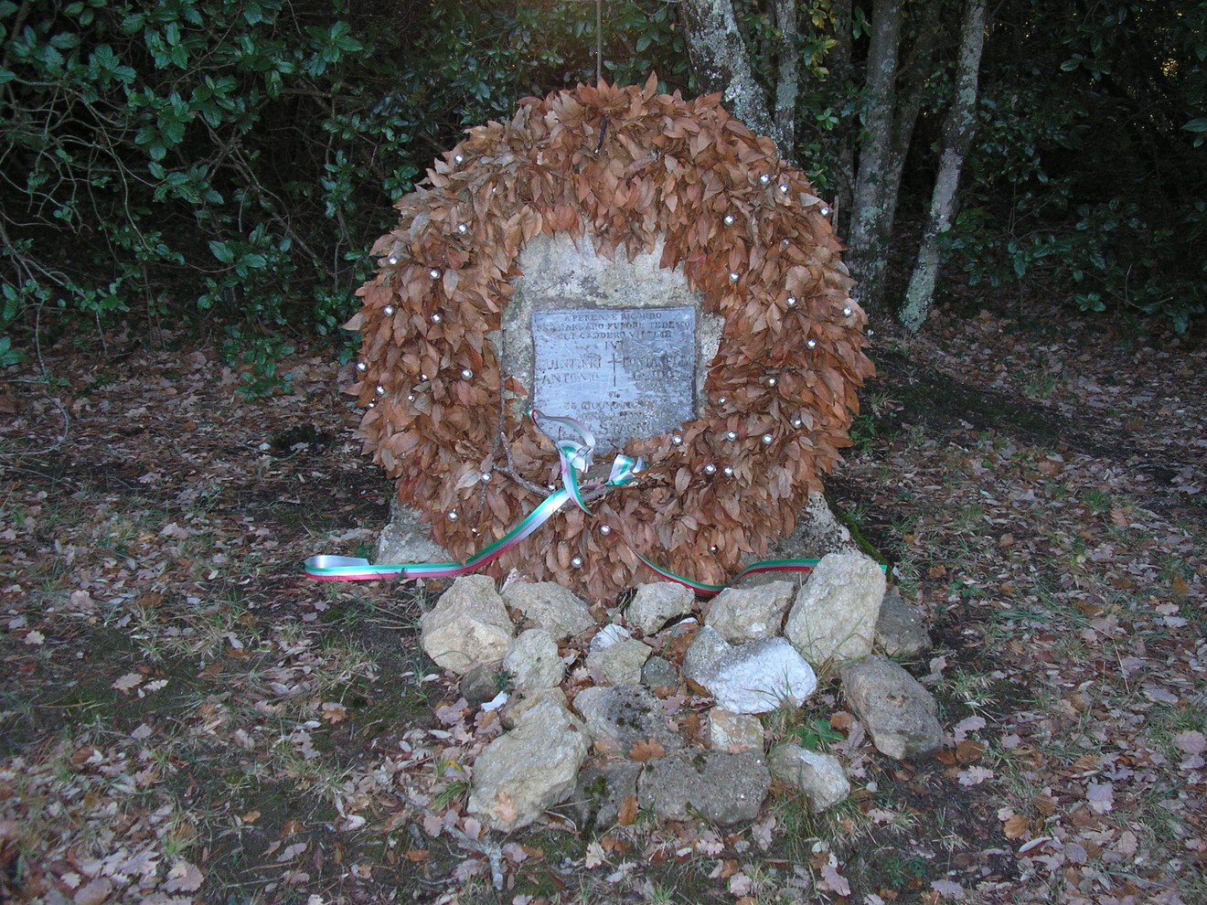 Cippo di San Vettore, monumento commemorativo circondato da foglie secche e decorazioni tricolori.