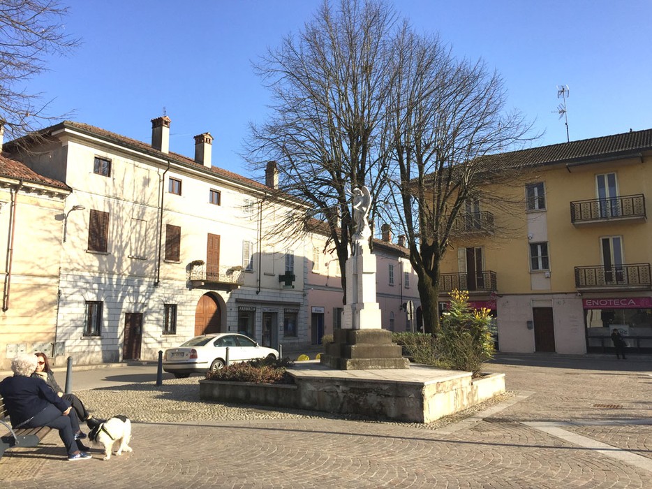 Monumento ai Caduti di Dorno, situato in una piazza tranquilla, circondato da edifici storici e alberi.