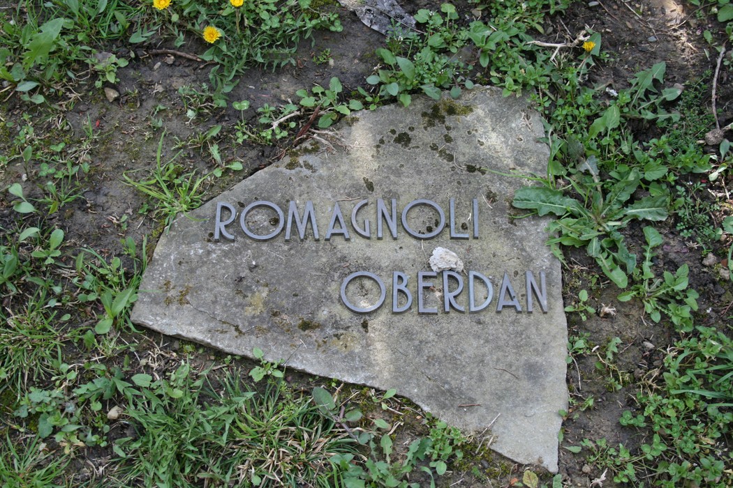 Monumento del cimitero di Stia, con iscrizioni su una pietra, immerso nel verde e nella natura circostante.
