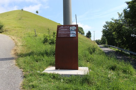 Pannello informativo lungo la Strada della battaglia di Fonteno, circondato da colline verdi e cielo sereno.