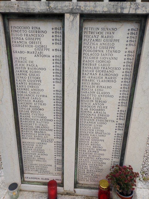 Monumento commemorativo con nomi incisi dei caduti per la libertà, circondato da fiori e candele.
