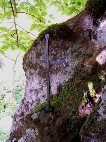 Croci di Carbonettoli: croce metallica affissa a una roccia, circondata da muschio e vegetazione lussureggiante.